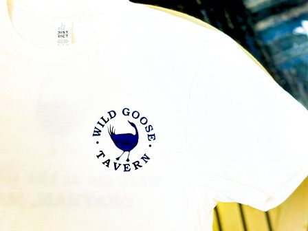 A white T-shirt with a logo on the chest that features a blue goose and the text 