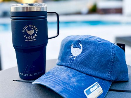 The image shows a travel mug and a blue baseball cap, both featuring a white bird logo and 