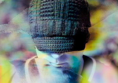 A person wearing a dark knit beanie hides their eyes, head slightly bowed, with blurred, colorful light streaks creating a dreamy, moody vibe.