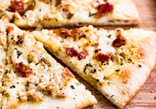 Two slices of herb-speckled flatbread/pizza with red pepper and melted cheese on a rustic wooden board.
