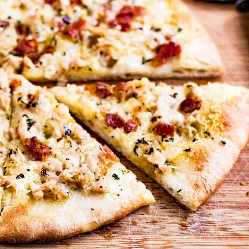 Two slices of herb-speckled flatbread/pizza with red pepper and melted cheese on a rustic wooden board.